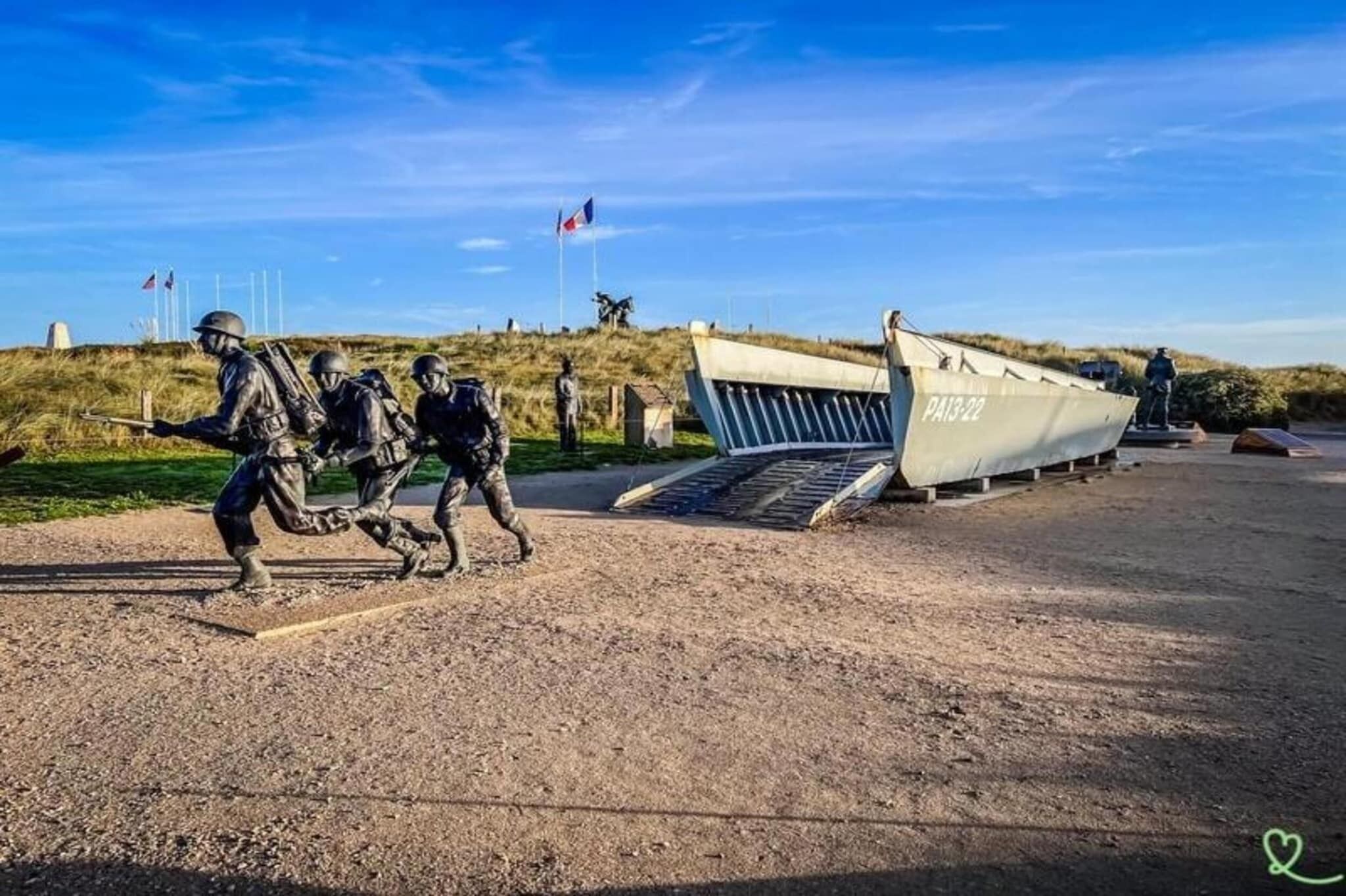 A military memorial with a statue of soldiers, a boat labeled "PA13-22", and a flagpole with flags.