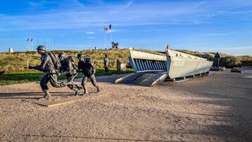 A military memorial with a statue of soldiers, a boat labeled "PA13-22", and a flagpole with flags.