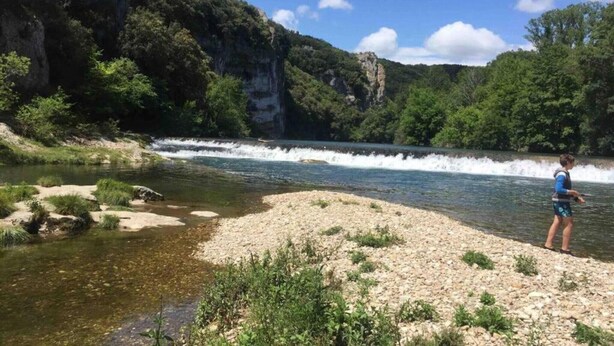 Un paysage naturel comprenant une rivière, une rive rocheuse et une végétation luxuriante.