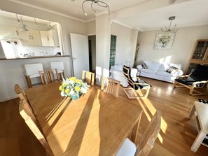 Un ampio soggiorno con tavolo da pranzo in legno, divani bianchi e angolo cottura con pensili e frigorifero.