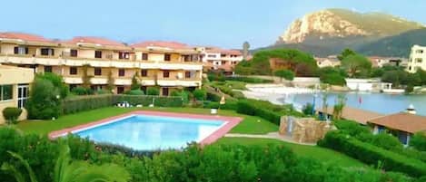 A hotel with a swimming pool surrounded by lush greenery and a mountain in the background.