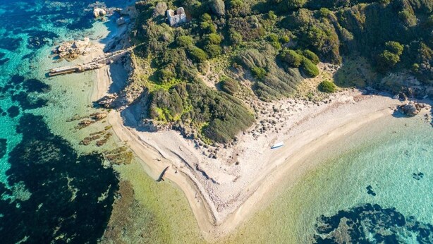 Vista aérea de una zona costera con aguas azul turquesa, una playa arenosa y densa vegetación verde.