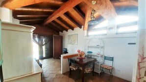 Un comedor con mesa y sillas de madera, un armario blanco y un techo con vigas a la vista.