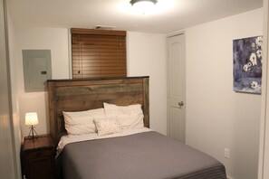 A bedroom with a wooden headboard, a bed with patterned bedding, a nightstand with a lamp, and a painting on the wall. - Belas Resort (Willis)