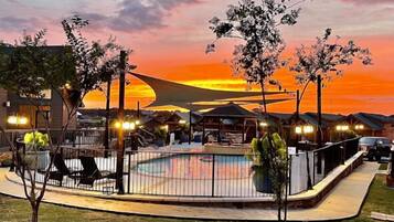 A pool area with a sunset view, surrounded by buildings and trees.