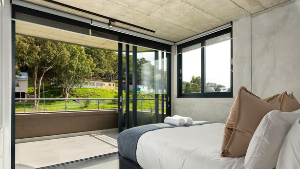 A modern bedroom with a large bed, a balcony with glass doors, and a view of a green landscape. - FortyOnL 810 (Cape Town)