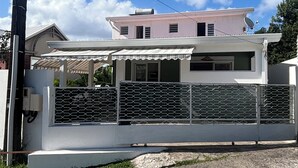 Une maison à deux étages, avec une façade blanche, une clôture en métal et une antenne parabolique.