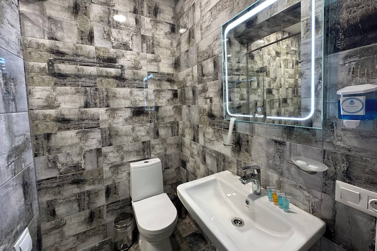 Une salle de bain avec un mur en marbre, un lavabo blanc et des toilettes.