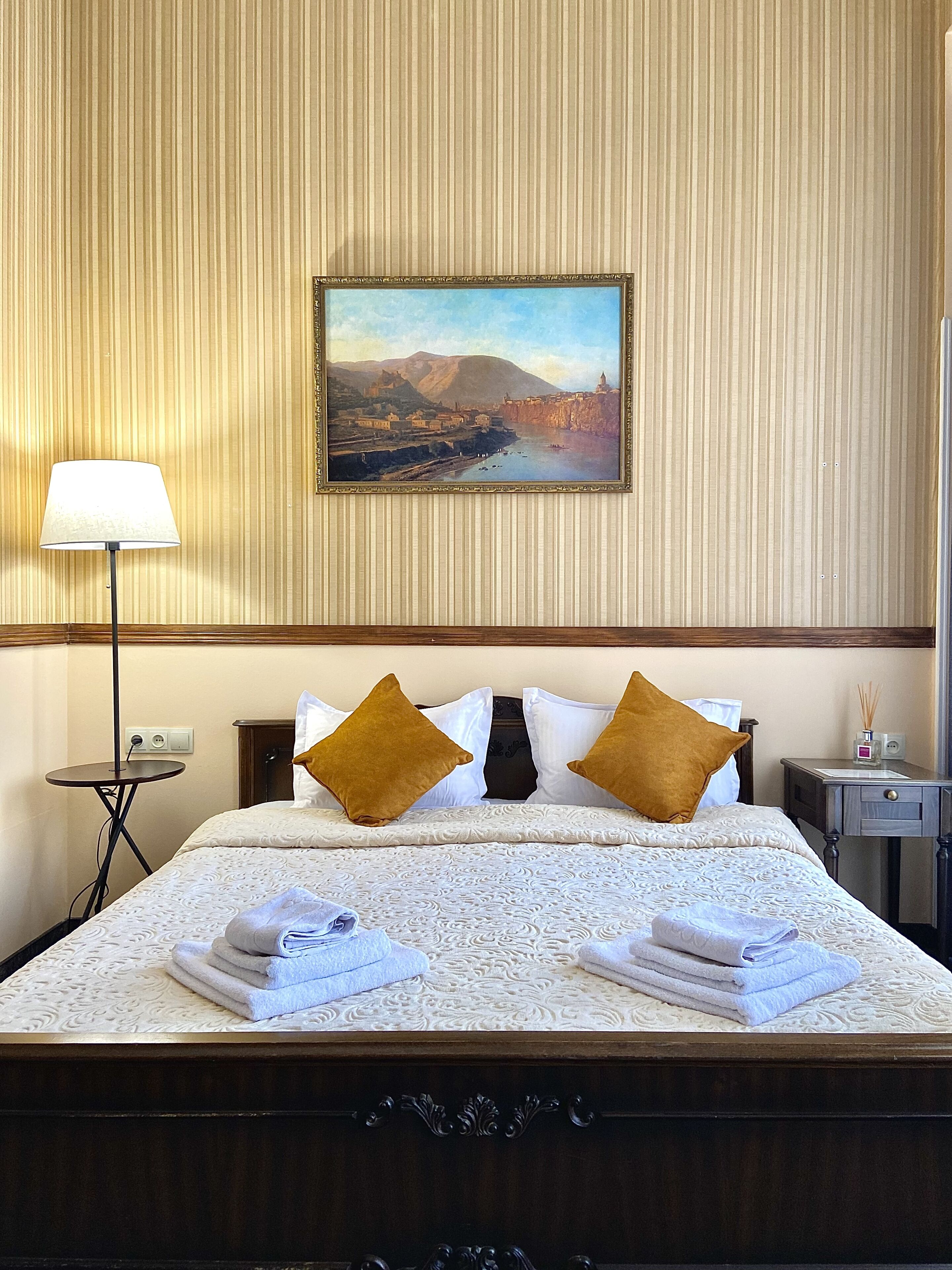 A hotel room with a large bed, a painting on the wall, a lamp, and a small table.