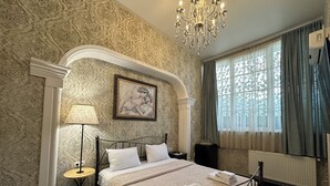 Ein Schlafzimmer mit einem großen Bett, einer Kristallleuchter, einem gerahmten Kunstwerk, einem Fenster mit Vorhängen und einer Heizkörper.