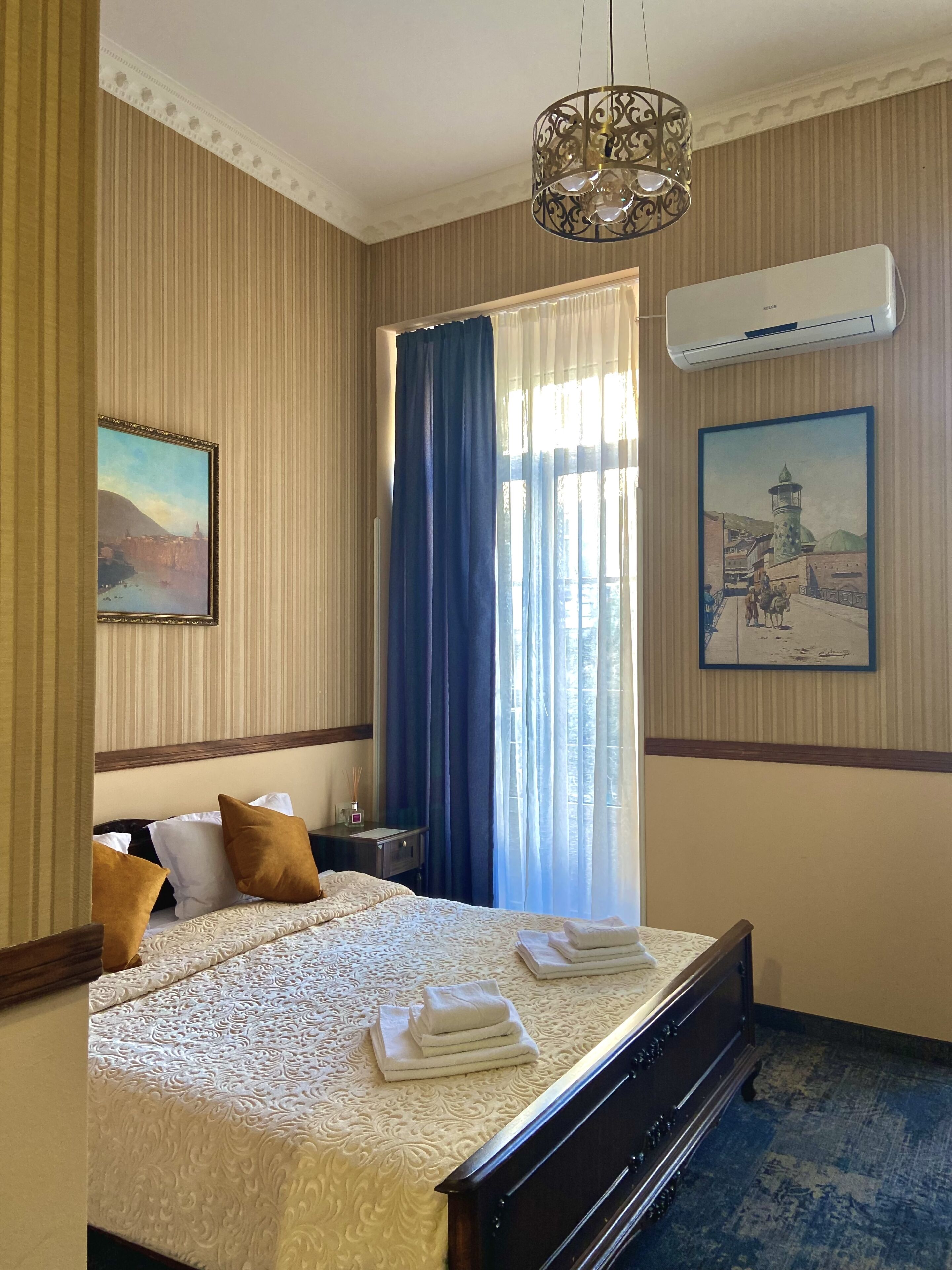 A hotel room with a large bed, a nightstand, a lamp, and two paintings on the walls.
