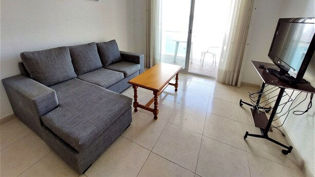 Una sala de estar con un sofá gris, una mesa de centro de madera y un televisor sobre un mueble.
