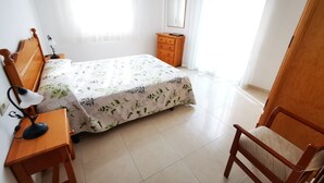 Un dormitorio con cama, cómoda de madera, escritorio con lámpara y silla.