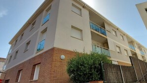 Un edificio residencial de varios pisos con fachada plana, balcones y base de ladrillo.