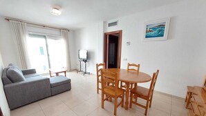 Una sala de estar con un sofá, una mesa de comedor con sillas, un televisor sobre un mueble bajo y un cuadro en la pared.