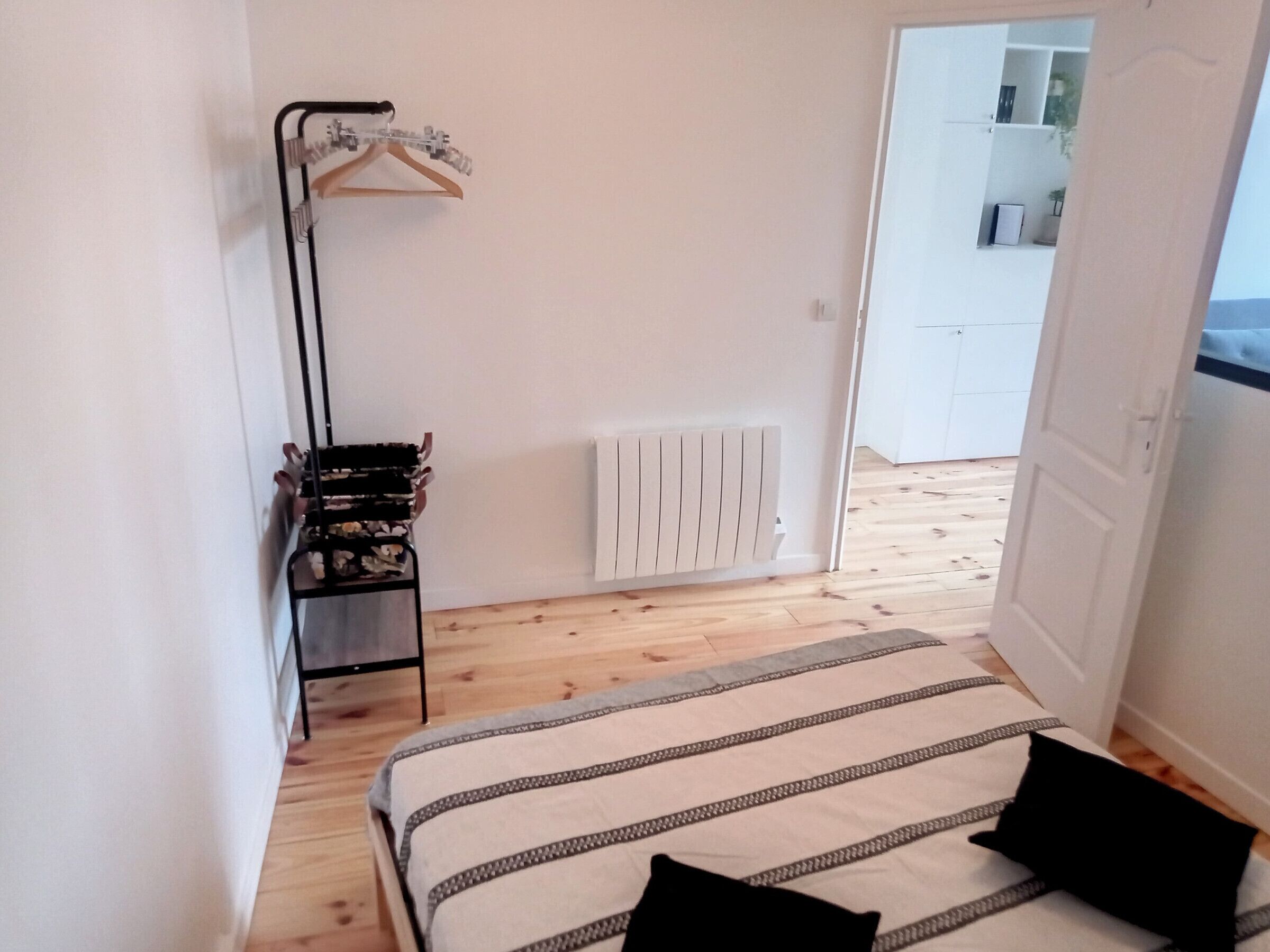 A bedroom with a bed, a radiator, a wardrobe, and a hanging rack.