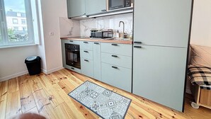 Una cucina compatta con mobili grigi, un forno a microonde, un lavandino e un piccolo forno. Si vede una finestra con vista sugli edifici.