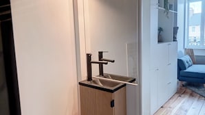 Un bagno moderno con box doccia in vetro, un armadietto in legno e un divano blu nella zona soggiorno adiacente.