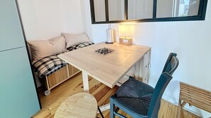Una stanza piccola con un tavolo di legno, una sedia, un divano con cuscini, una lampada e uno specchio a parete.