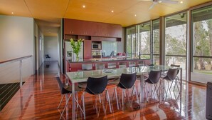 Une cuisine moderne avec une table et des chaises en verre, un ventilateur de plafond et de grandes fenêtres offrant une vue sur l’extérieur.