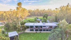 Une grande maison moderne, dotée d’une vaste pelouse et entourée d’arbres denses.