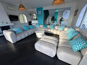 Un salon moderne avec un canapé d’angle, une table basse ronde et un coin repas comprenant une table et des chaises blanches.