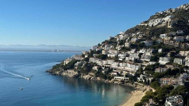 A coastal town with buildings on a hillside overlooking a beach.