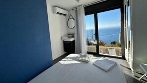 A bedroom with a bed, a bathroom with a sink, and a view of the sea.
