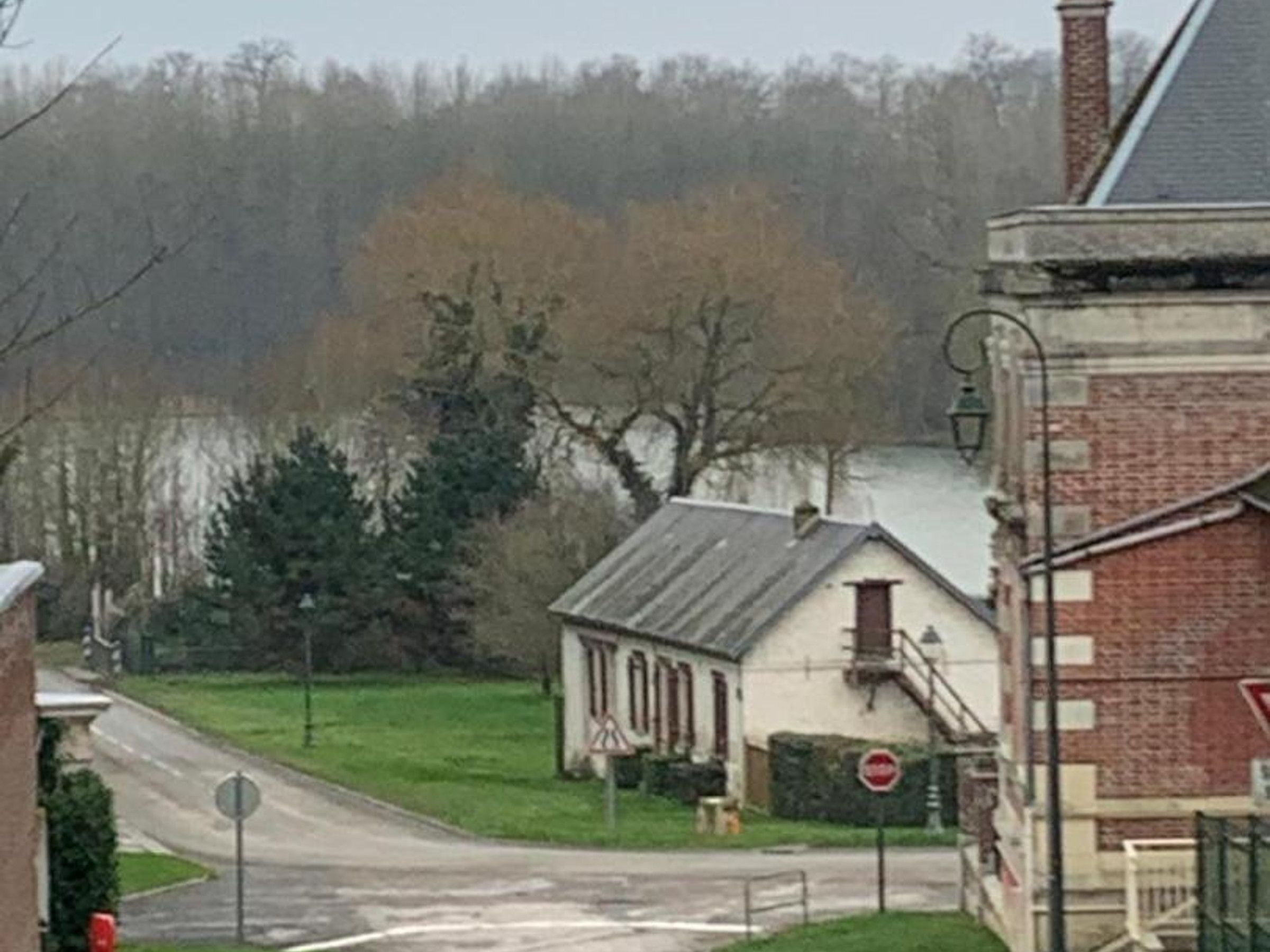 Eine Landstraße mit einem Stoppschild, ein kleines Gebäude mit weißer Fassade und ein Ziegelhaus mit Schornstein.