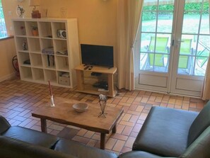 Un salon comprenant un canapé, une table basse, un téléviseur posé sur un meuble et une étagère contenant divers objets.