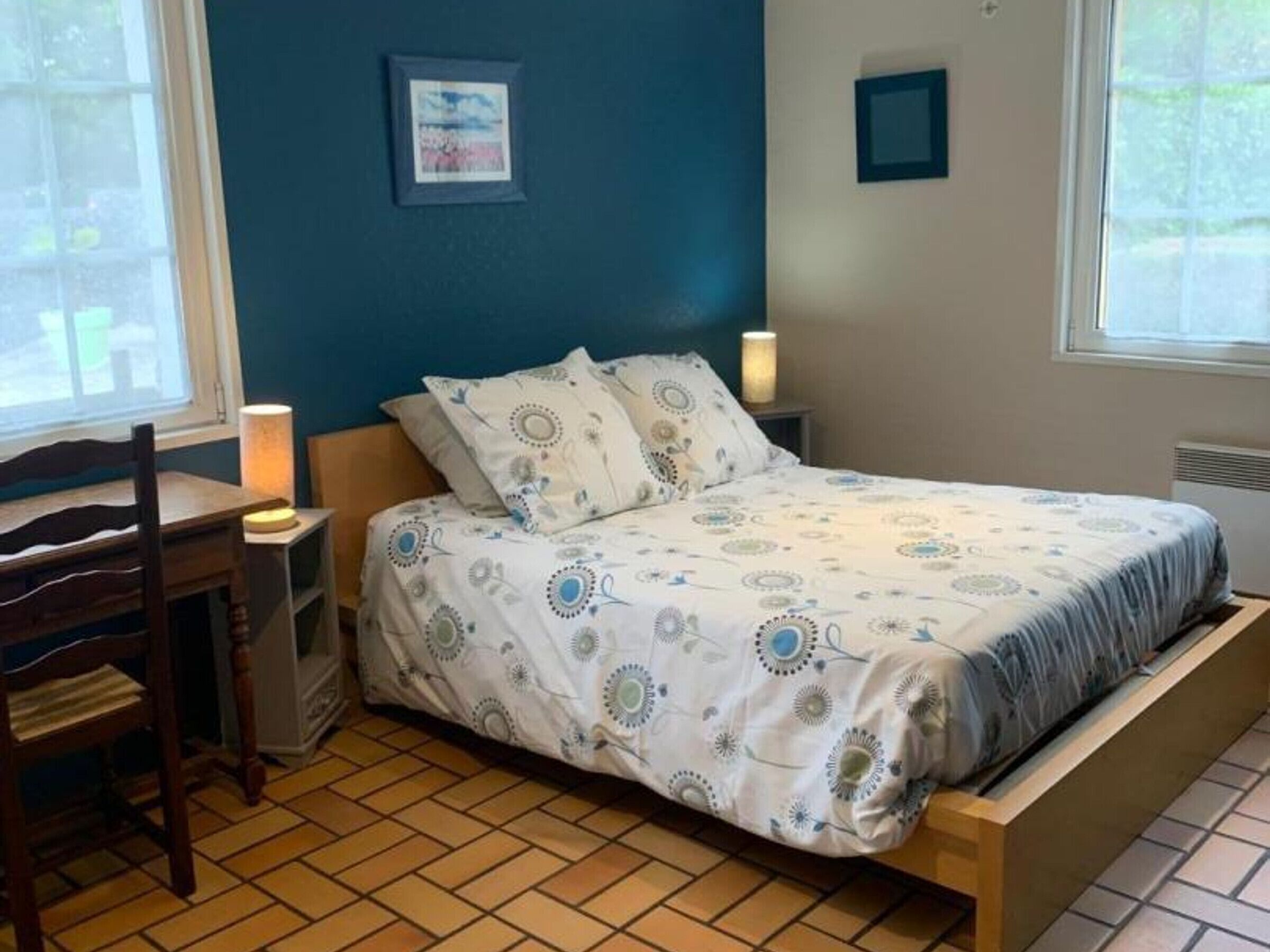 Ein Schlafzimmer mit einem Bett, einem Schreibtisch, einem Stuhl, einem Nachttisch mit Lampe und einem Fenster.
