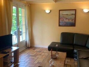 Un salon avec un canapé, un téléviseur posé sur un meuble, un tableau accroché au mur et une fenêtre avec des rideaux.