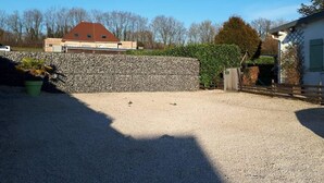 A gravel driveway leading to a stone wall, a building with a red roof, and a house with a white exterior. - Single-storey house, pets welcome - 6 guests (Caulaincourt)