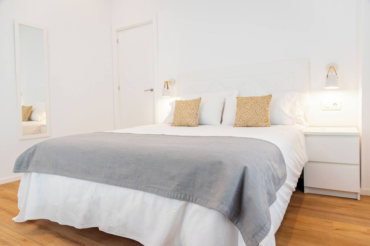 A neatly arranged bedroom with a large bed, bedside tables, and a mirror.