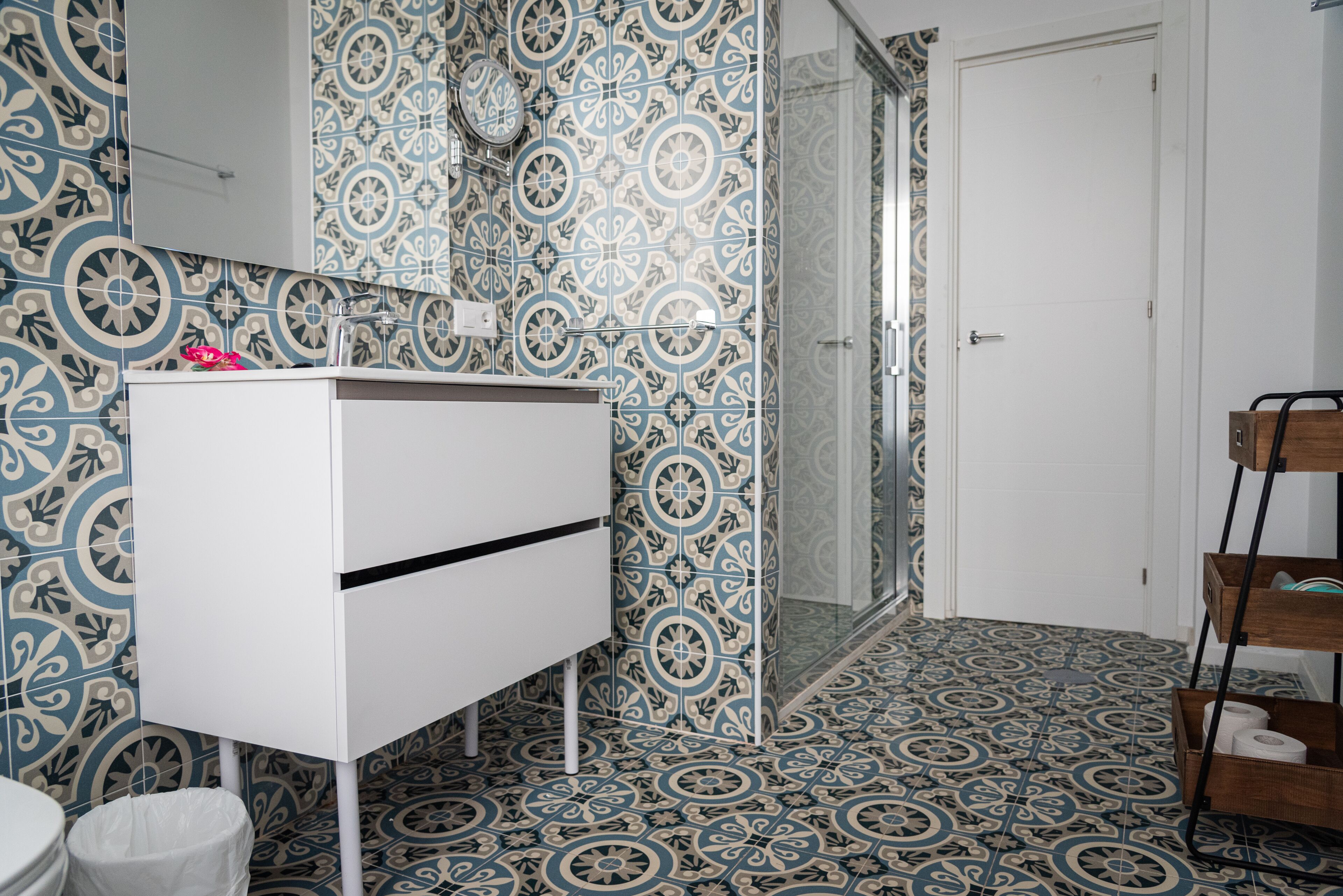 A bathroom with patterned tiles, a white vanity, a mirror, and a shower area.