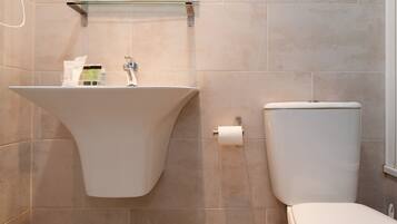 A bathroom with a freestanding sink, toilet, and a glass shelf above the sink.