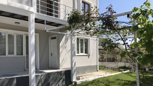 A modern two-story house with a covered porch, a small garden, and a visible door. - Bavella House Pamukkale (Denizli)
