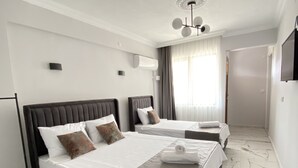A modern hotel room with two beds, marble flooring, a ceiling fan, and a TV on the wall. - Bavella House Pamukkale (Denizli)