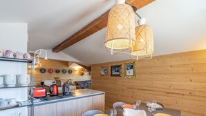 Ett modernt kök med trädetaljer, en matplats med ett bord för fyra personer och en köksö med vattenkokare och brödrost.