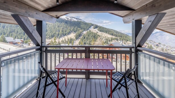 En träveranda med ett bord och stolar, med utsikt över ett bergigt landskap.