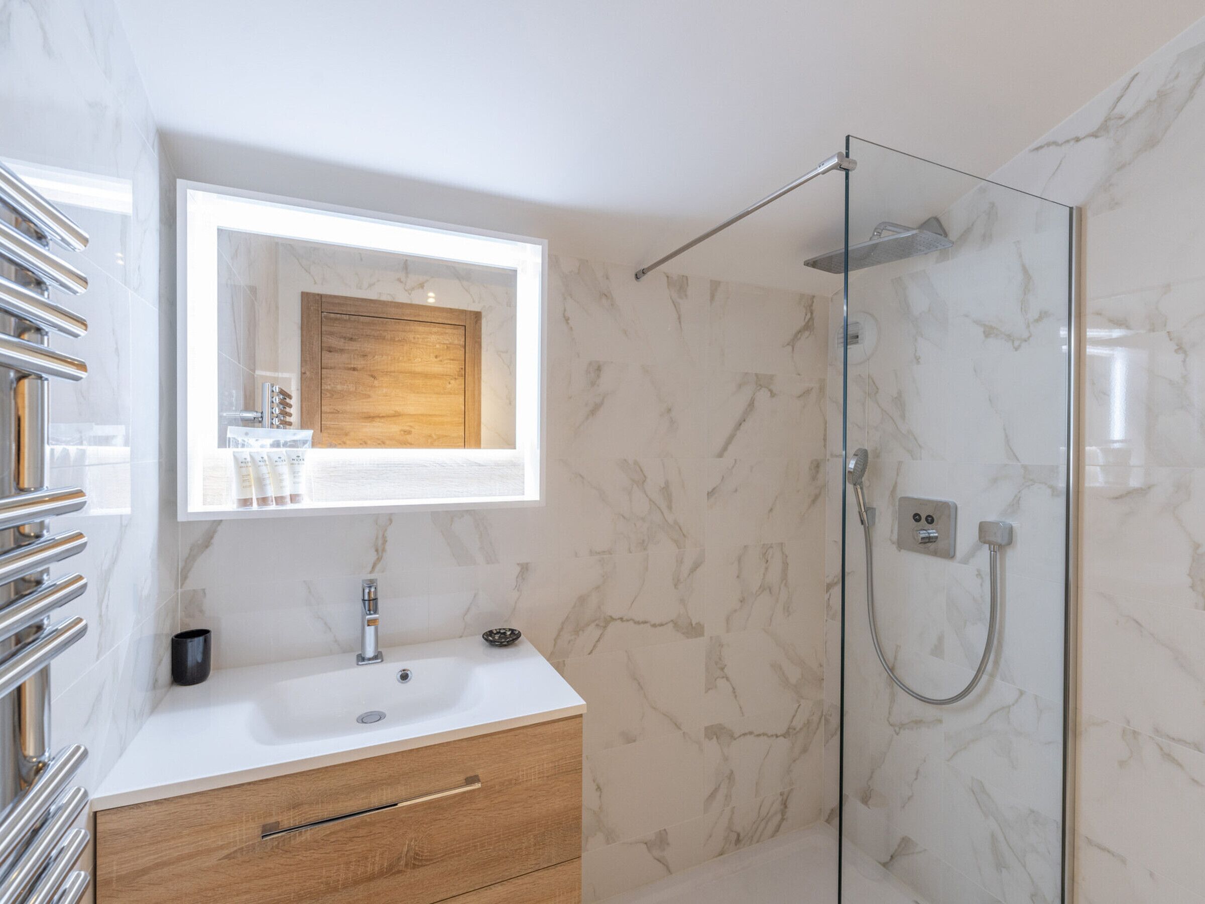 A modern bathroom with a glass shower enclosure, a vanity with a mirror, and a marble-tiled wall.