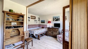 Ein gemütliches Zimmer mit einem Bücherregal aus Holz, einem Bett mit karierter Bettdecke, einem Schreibtisch mit Lampe und einem Fernseher.