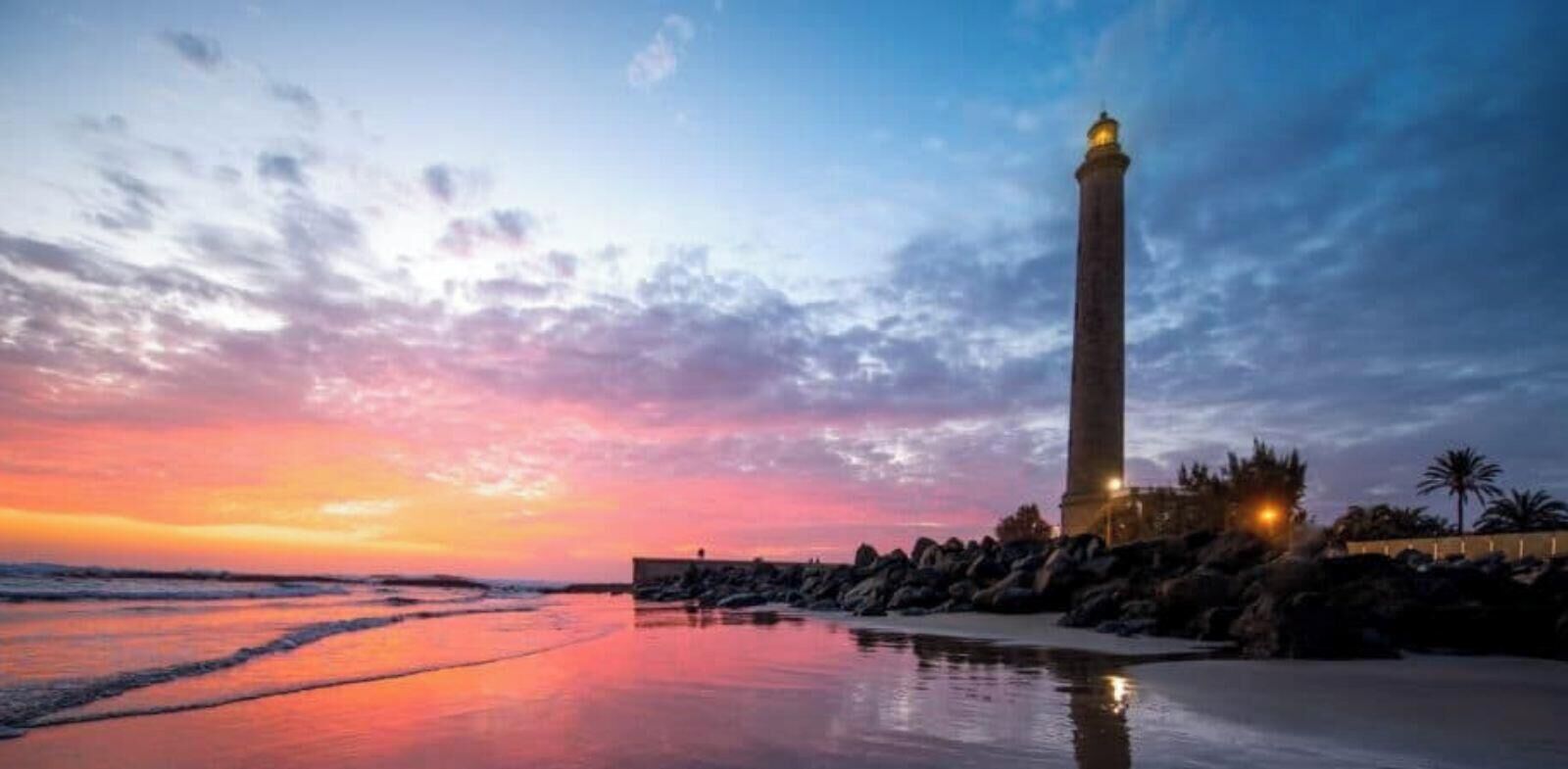 Escena costera con un alto faro, costa rocosa y cielo al atardecer.