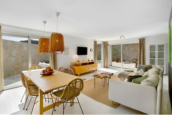 A modern living room with a dining area, a sofa, a TV, and a stone wall. - Luxury Boho Villa • Heated Pool • Rooftop • Panoramic Sea View • Amadores (Mogán)