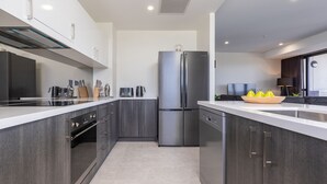 A modern kitchen with a stainless steel refrigerator, dark cabinetry, and a white countertop. - Cove 601 - Luxury living in Forster. (Forster)