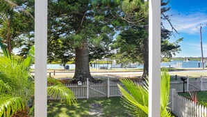 A gazebo with a white picket fence, a large tree, and a view of a water body with boats. - River Tonic - stunning views of the Myall River (Tea Gardens)