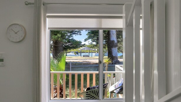 A view from a room with a white door, a clock on the wall, and a balcony overlooking a park with a gazebo and trees. - River Tonic - stunning views of the Myall River (Tea Gardens)