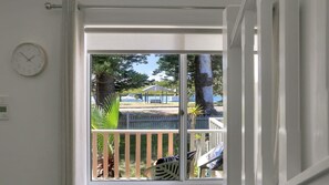 Blick von einem Zimmer mit weißer Tür, einer Uhr an der Wand und einem Balkon mit Blick auf einen Park, der eine Laube und Bäume beinhaltet.