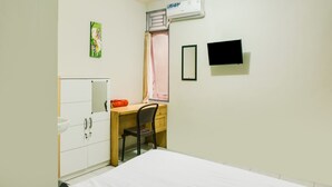 Un dormitorio con cama, un escritorio con silla, armario, ventana con cortinas, aire acondicionado y televisor en la pared.