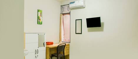 A bedroom with a bed, a desk with a chair, a wardrobe, a window with curtains, an air conditioner, and a TV on the wall.